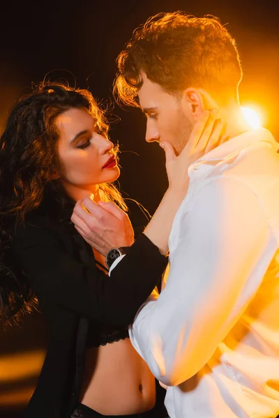 Seductive woman in blazer touching boyfriend on black with back light — Stock Photo