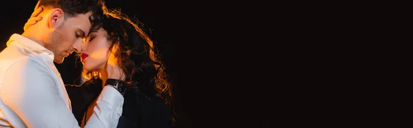 Tiro panorâmico de homem tocando mulher encaracolado com olhos fechados isolado em preto — Fotografia de Stock