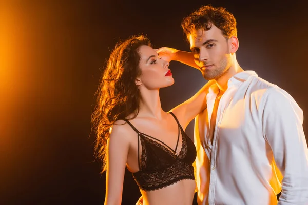 Curly woman in lace bra looking at man in shirt on black — Stock Photo