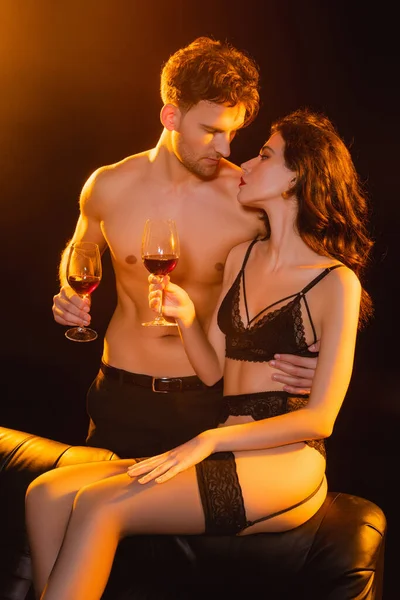 Homem muscular e mulher sedutora segurando copos de vinho tinto enquanto olham um para o outro em preto — Fotografia de Stock