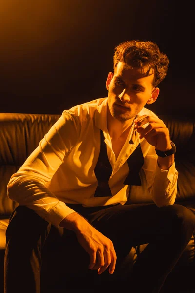 Uomo in giacca e cravatta con sigaro e seduto sul divano isolato su nero — Foto stock
