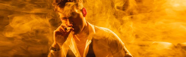 Horizontal image of man in suit holding cigar and looking at camera on black with smoke — Stock Photo