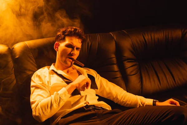 Confident man in suit smoking cigar and looking at camera on black — Stock Photo