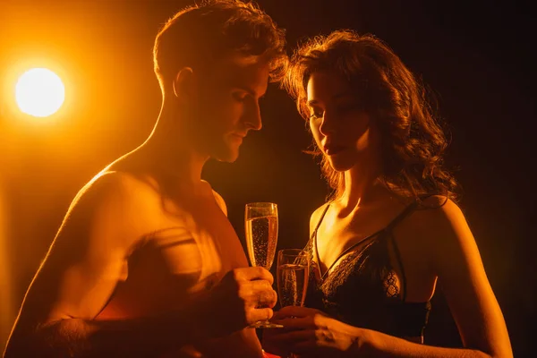 Сексуальная пара, держащая бокалы с шампанским на черном с задним светом — стоковое фото