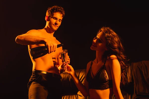 Homme musclé tenant bouteille avec champagne près femme heureuse avec verre isolé sur noir — Photo de stock