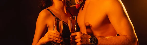 Horizontal crop of seductive woman holding fresh strawberry near muscular man with glass of champagne on black — Stock Photo