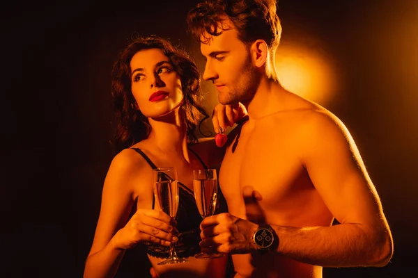 Curly woman holding fresh strawberry near shirtless man with glass of champagne on black — Stock Photo