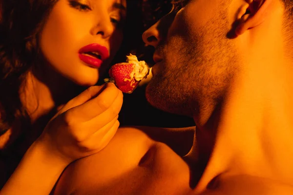 Sexy mujer con labios rojos alimentación sin camisa hombre con crema batida en fresa fresca - foto de stock