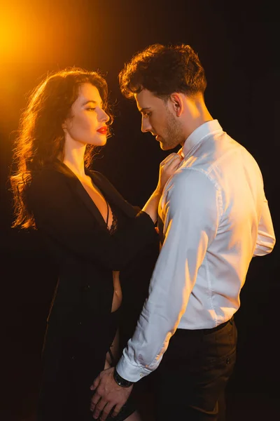 Illuminazione su donna seducente che tocca la camicia di uomo su nero — Foto stock