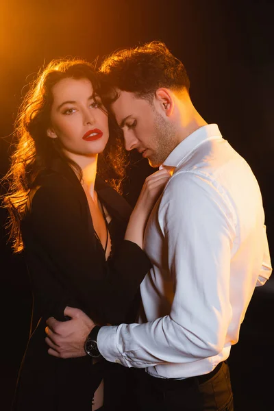Curly woman in jacket touching man in shirt on black — Stock Photo