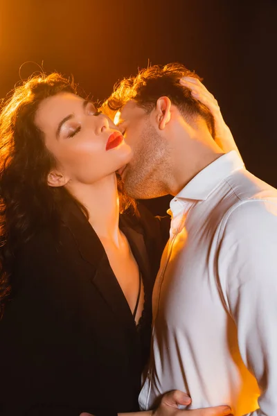 Man in shirt kissing woman with closed eyes in jacket on black — Stock Photo