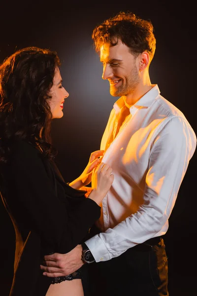 Man in suit looking and hugging curly woman in blazer on black — Stock Photo