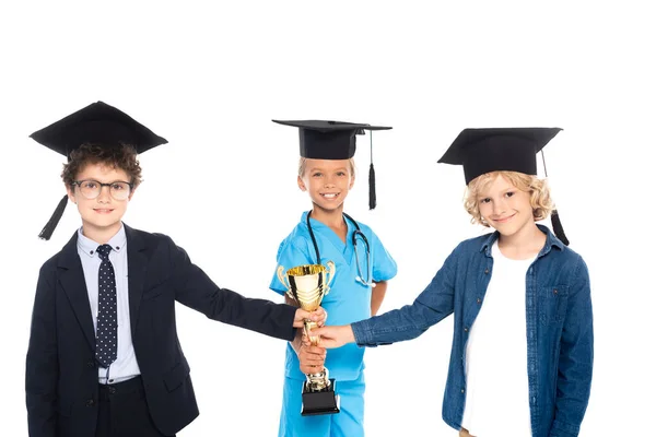 Children in graduation caps dressed in costumes of different professions holding golden trophy isolated on white — Stock Photo