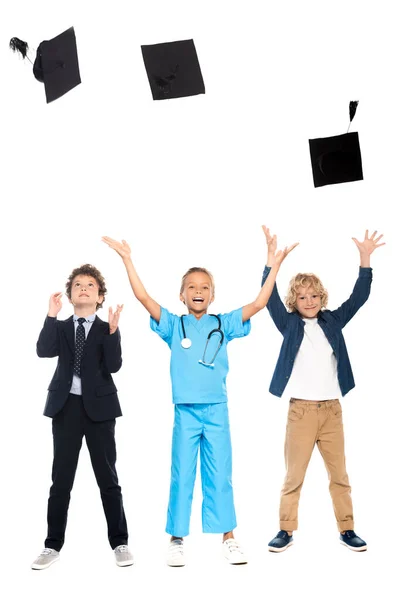 Kids dressed in costumes of different professions throwing in air graduation caps isolated on white — Stock Photo