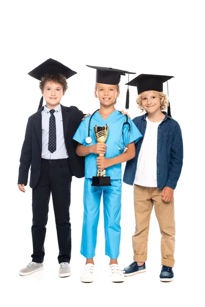 Enfants en casquettes de graduation vêtus de costumes de différentes professions tenant trophée isolé sur blanc — Photo de stock