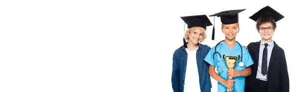Panoramic crop of children in graduation caps dressed in costumes of different professions holding trophy isolated on white — Stock Photo
