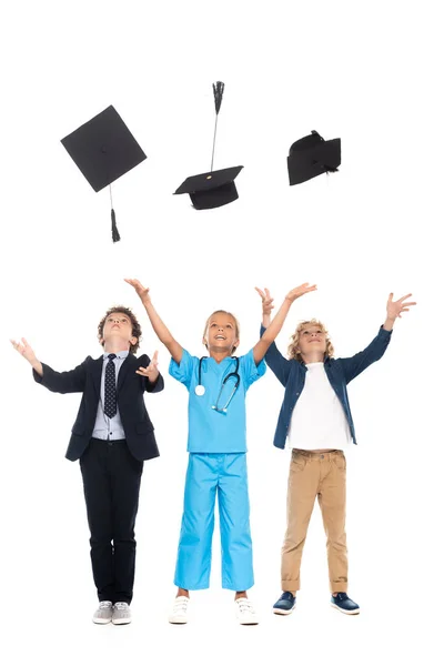 Children dressed in costumes of different professions throwing in air black graduation caps isolated on white — Stock Photo
