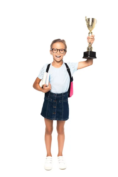 Збуджена школярка в окулярах тримає книги і золотий трофей ізольовано на білому — стокове фото