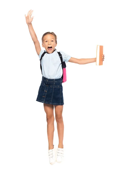 Schoolgirl in glasses jumping and screaming while holding book isolated on white — Stock Photo