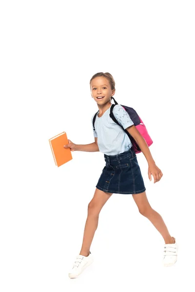 Niño emocionado en gafas sosteniendo libro mientras camina aislado en blanco - foto de stock