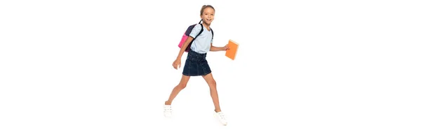 Горизонтальное изображение возбужденного школьника в очках, держащего книгу во время ходьбы изолированной на белом — стоковое фото