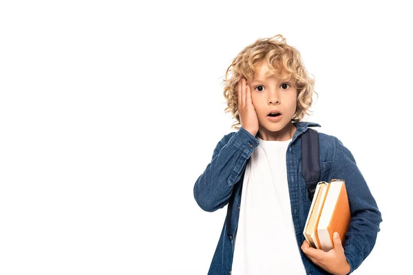 Schockierter blonder Schuljunge hält Bücher und berührt Gesicht isoliert auf weißem Hintergrund — Stockfoto
