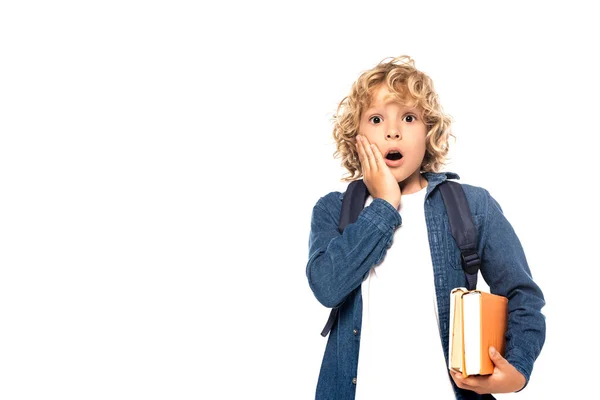 Schockiertes blondes Schulkind berührt Gesicht und hält Bücher isoliert auf weißem Papier — Stockfoto