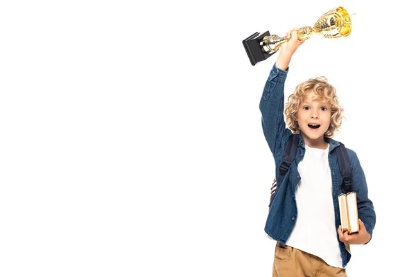 Excitado colegial rubia sosteniendo trofeo de oro y libros aislados en blanco - foto de stock