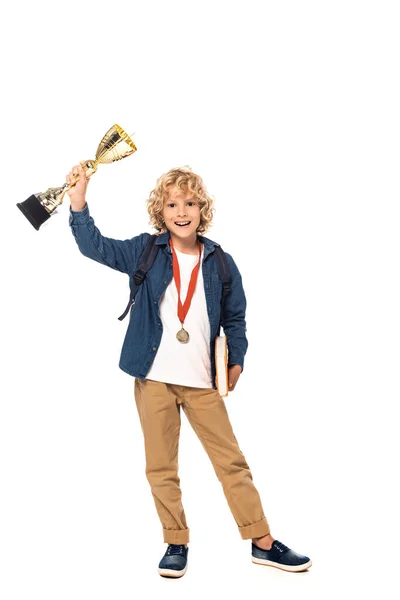 Écolier blonde avec médaille d'or tenant trophée et livre isolé sur blanc — Photo de stock