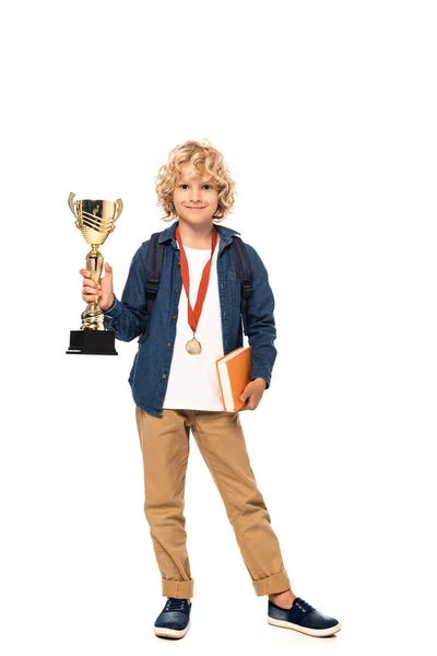 Estudante loira encaracolado com medalha de ouro segurando troféu e livro isolado em branco — Fotografia de Stock