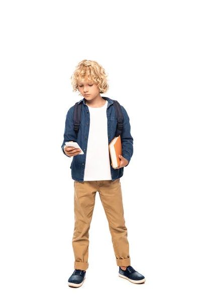 Blonde écolier tenant livre et en utilisant smartphone isolé sur blanc — Photo de stock