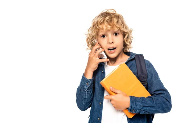 Überraschter blonder Schüler hält Buch in der Hand und spricht auf Smartphone isoliert auf weißem Grund — Stockfoto