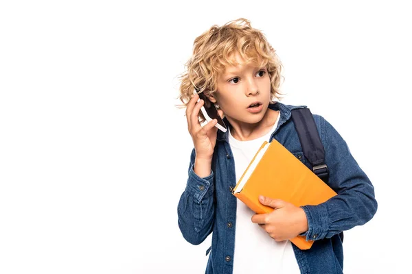 Curious schoolboy holding book and talking on smartphone isolated on white — Stock Photo