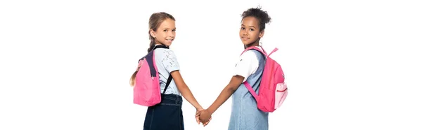 Horizontales Bild von multikulturellen Klassenkameraden mit Rucksäcken, die sich an den Händen halten und die Kamera isoliert auf Weiß betrachten — Stockfoto
