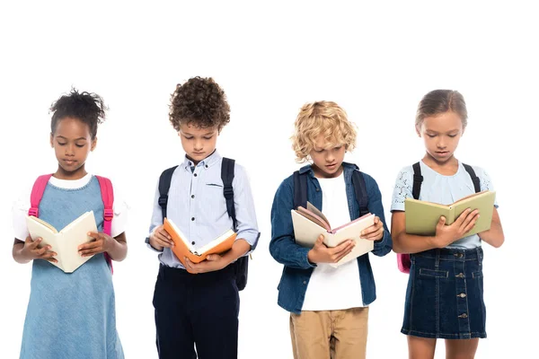 Multicultural and curly schoolkids reading books isolated on white — Stock Photo