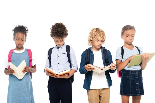 Мультикультурні школярі з рюкзаками читають книги ізольовані на білому — стокове фото