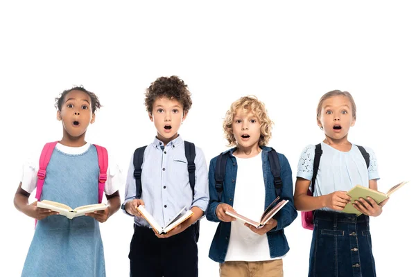 Escolares multiculturales y sorprendidos sosteniendo libros aislados en blanco - foto de stock