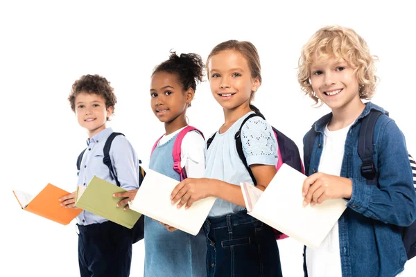 La concentration sélective des écoliers multiculturels avec des sacs à dos contenant des livres isolés sur blanc — Photo de stock