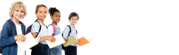 Horizontal image of multicultural schoolkids with backpacks holding books isolated on white — Stock Photo