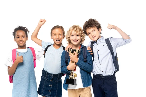 Écoliers multiculturels célébrant triomphe près garçon bouclé avec trophée isolé sur blanc — Photo de stock