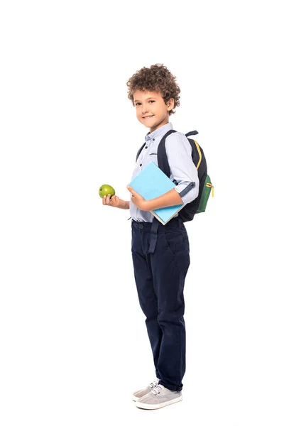 Curly schoolboy with backpack and book holding apple isolated on white — Stock Photo