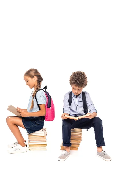 Escolares sentados en libros y leyendo aislados en blanco - foto de stock