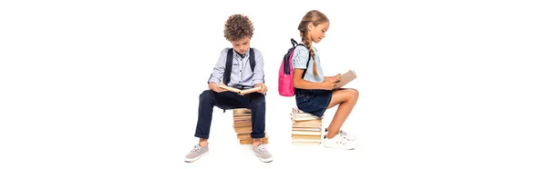 Panoramic shot of schoolkids sitting on books and reading isolated on white — Stock Photo