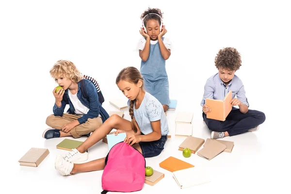 Schulkinder sitzen neben Büchern, Äpfeln und afrikanisch-amerikanischen Kind in drahtlosen Kopfhörern isoliert auf weiß — Stockfoto