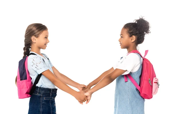 Vista lateral de escolares multiculturales tomados de la mano aislados en blanco - foto de stock