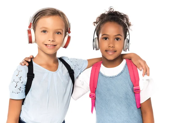 Multikulturelle Schulkinder hören Musik in drahtlosen Kopfhörern, während sie die Kamera isoliert auf weiß anschauen — Stockfoto