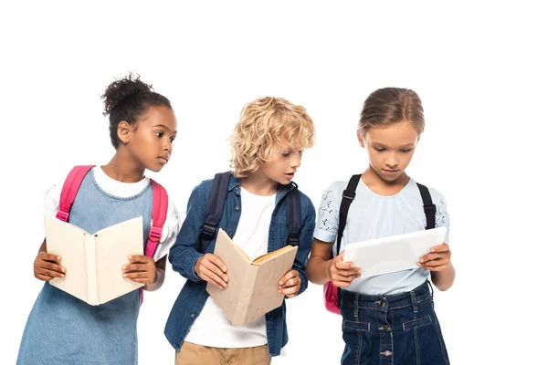 Scolaretta afroamericana e studentessa bionda con libri che guardano tablet digitale in mano di compagno isolato su bianco — Foto stock