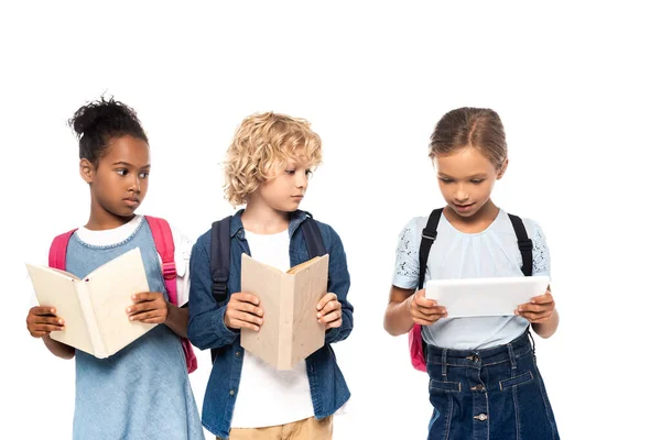 Scolaretta afroamericana e scolaretto riccio con libri guardando tablet digitale in mano di compagno isolato su bianco — Foto stock