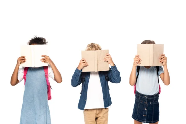 Multicultural schoolgirls and schoolboy covering faces with books isolated on white — Stock Photo