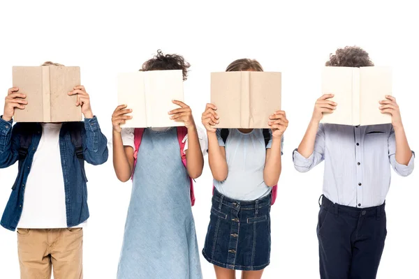 Multikulturelle Schulmädchen und Schuljungen, die Gesichter mit Büchern bedecken, isoliert auf weiß — Stockfoto